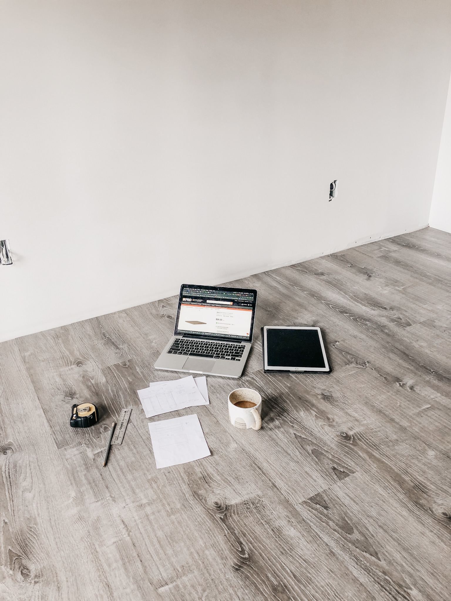 image of computer, measuring tape and papers spread out on floor of unfinished room.
